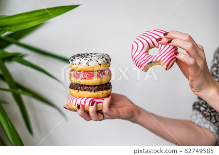 Female holds in hand colorful stack of glazed donuts. White background. Top view. Copy space Female holds in hand colorful stack of glazed donuts. White background. Top view. Copy space 82749585