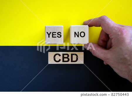Man holds a cubes with word 'no'. Wooden cubes with word 'yes' and word 'plan'. Beautiful yellow and black background. Copy space. Concept of CBD legalization and use. 82750443