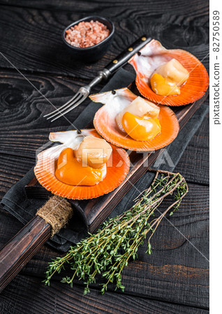 Scallops raw Shellfish on a wooden board with herbs. Black wooden background. Top view Scallops raw Shellfish on a wooden board with herbs. Black wooden background. Top view 82750589