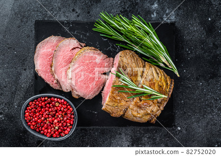 Roast beef fillet Tenderloin meat on a marble board. Black background. Top view 82752020