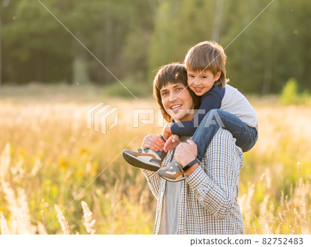 Cute boy and his father. Happy kid smiles. Dad and son on field at golden sunset hour at autumn season. Family life. 82752483