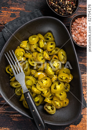 Preserved Jalapenos, pickled and sliced in plate . Dark Wooden background. Top view Preserved Jalapenos, pickled and sliced in plate . Dark Wooden background. Top view 82754176