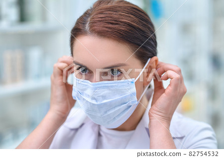 Woman working in pharmacy putting on protective mask 82754532