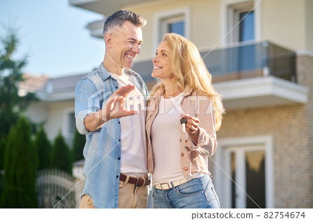 Woman with keys looking at husband with house sign Woman with keys looking at husband with house sign 82754674