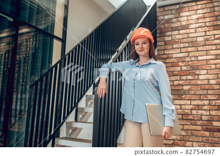 Smiling woman in safety helmet with laptop 82754697