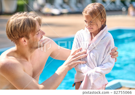 A young man wdrying his kid with a towel near the pool A young man wdrying his kid with a towel near the pool 82755066