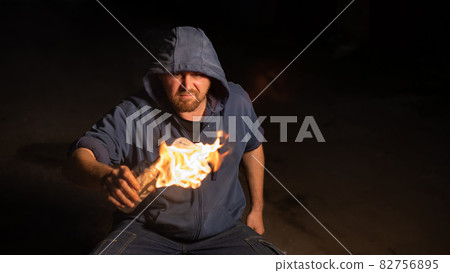The man in the hood is holding a burning bottle. Molotov cocktail. The man in the hood is holding a burning bottle. Molotov cocktail. 82756895