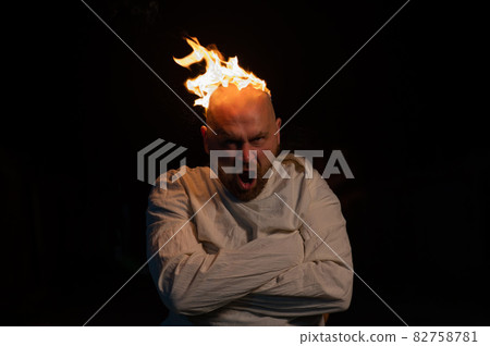 Bald man in a straitjacket with a burning head on a dark background. 82758781