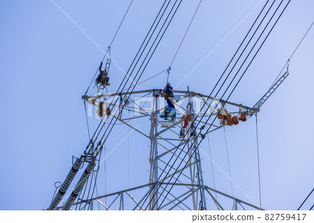 Power company workers perform maintenance and inspection of transmission lines at the top of transmission towers 82759417