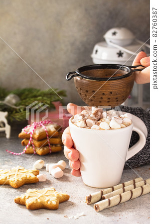 Female hands holding a cup of hot cocoa with marshmallows, Christmas sweets on a stone countertop. Copy space. Female hands holding a cup of hot cocoa with marshmallows, Christmas sweets on a stone countertop. Copy space. 82760387