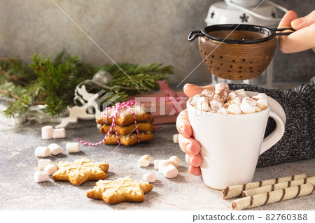 Female hands holding a cup of hot cocoa with marshmallows, Christmas sweets on a stone countertop. Copy space. Female hands holding a cup of hot cocoa with marshmallows, Christmas sweets on a stone countertop. Copy space. 82760388