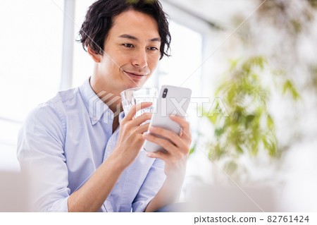 A young man looking at a smartphone screen with a smile A young man looking at a smartphone screen with a smile 82761424