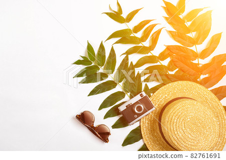 Straw hat with green leaves and old camera on white background, Summer background. Top view. Sun flare 82761691