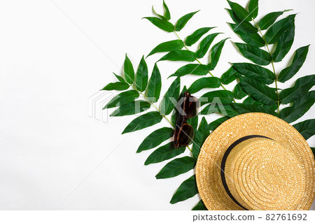 Green leaf branches and straw haton white background. flat lay, top view 82761692
