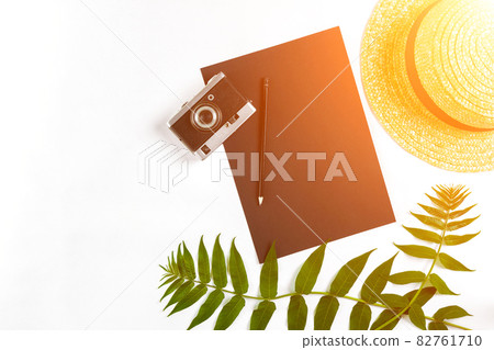 Straw hat with green leaves and old camera on white background, Summer background. Top view. Sun flare 82761710