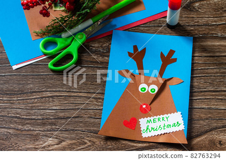 Merry greeting card with a Christmas deer on a wooden table. Handmade. Children's creativity project, crafts, crafts for kids. Merry greeting card with a Christmas deer on a wooden table. Handmade. Children's creativity project, crafts, crafts for kids. 82763294