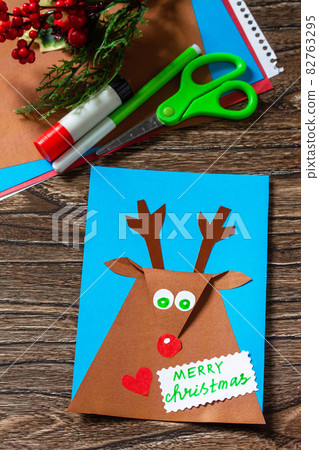 Merry greeting card with a Christmas deer on a wooden table. Handmade. Children's creativity project, crafts, crafts for kids. Merry greeting card with a Christmas deer on a wooden table. Handmade. Children's creativity project, crafts, crafts for kids. 82763295