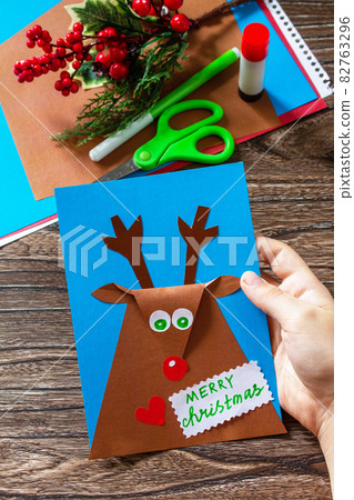 Merry greeting card with a Christmas deer on a wooden table. Handmade. Children's creativity project, crafts, crafts for kids. 82763296