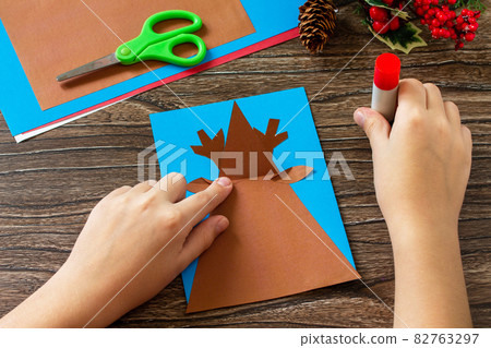 Instruction step 5. Merry greeting card with a Christmas deer on a wooden table. Handmade. Children's creativity project, crafts, crafts for kids. 82763297
