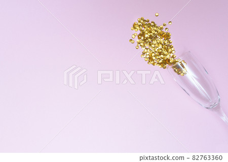 Glass of champagne with loose sparkles on a pink background and place for text. Holiday and celebration concept. New Year. Copy space. 82763360