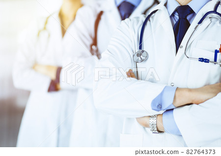 Group of modern doctors standing as a team with crossed arms and stethoscopes in a sunny hospital office. Physicians ready to examine and help patients. Medical help, insurance in health care, best 82764373