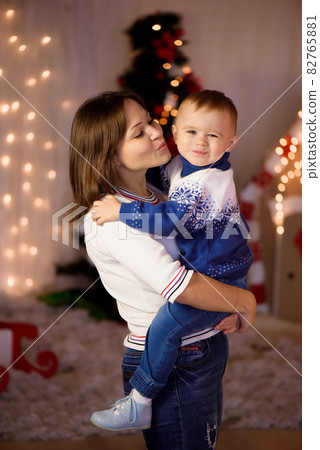 Cheerful mom and her cute son boy having fun near tree indoors. Loving family in christmas room. Cheerful mom and her cute son boy having fun near tree indoors. Loving family in christmas room. 82765881