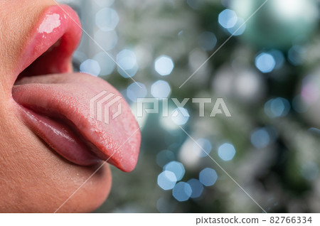 Close-up of large plump female lips against a background of christmas decorations. Close-up of large plump female lips against a background of christmas decorations. 82766334
