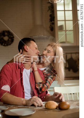 Christmas evening in the kitchen. Young people kiss and hug each other. 82767391