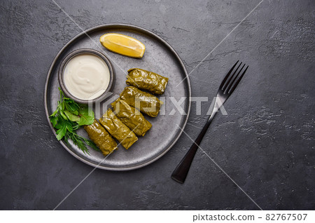 Dolma, parsley, saucepan with sour cream and lemon in black plate on dark table Dolma, parsley, saucepan with sour cream and lemon in black plate on dark table 82767507