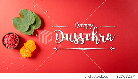 Happy Dussehra. Yellow flowers, green leaf and rice on red background. Dussehra Indian Festival concept. Happy Dussehra. Yellow flowers, green leaf and rice on red background. Dussehra Indian Festival concept. 82768237