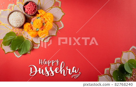Happy Dussehra. Yellow flowers, green leaf and rice on red background. Dussehra Indian Festival concept. Happy Dussehra. Yellow flowers, green leaf and rice on red background. Dussehra Indian Festival concept. 82768240