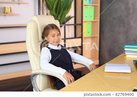 A child in a school uniform is posing in the classroom. A young schoolgirl looks at the camera. Girl in a lesson at school A child in a school uniform is posing in the classroom. A young schoolgirl looks at the camera. Girl in a lesson at school 82769400