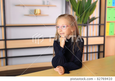 A child in a school uniform is posing in the classroom. A young schoolgirl looks at the camera. Girl in a lesson at school 82769410