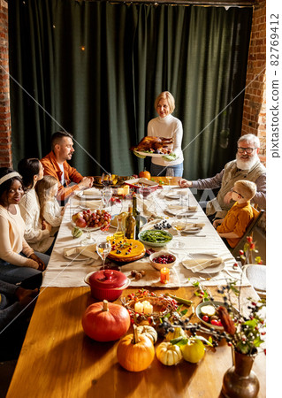 Happy Thanksgiving dinner party with family and friends with turkey and holiday traditional food, dishes on table. Happy Thanksgiving dinner party with family and friends with turkey and holiday traditional food, dishes on table. 82769412
