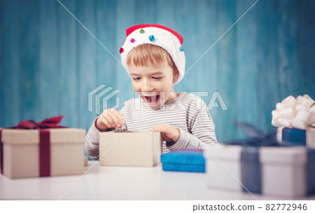 Cute child sitting at the table and opening giftboxes Cute child sitting at the table and opening giftboxes 82772946