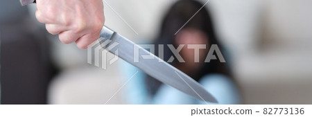 Aggressive man holds knife in hand against background of frightened woman Aggressive man holds knife in hand against background of frightened woman 82773136