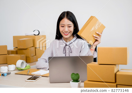 Young Asian woman business owner with many parcel boxes on the table happy online sales job, use your laptop, get an order from customers, take notes, and make arrangements for delivery by post Young Asian woman business owner with many parcel boxes on the table happy online sales job, use your laptop, get an order from customers, take notes, and make arrangements for delivery by post 82773146