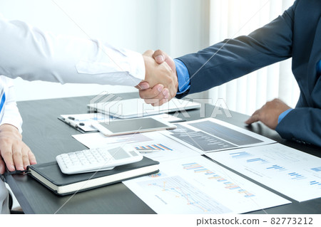 Shaking hand two business leaders talk about charts, financial graphs showing results are analyzing and calculating planning strategies, business success building processes Shaking hand two business leaders talk about charts, financial graphs showing results are analyzing and calculating planning strategies, business success building processes 82773212
