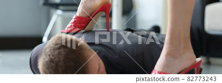 Woman in red shoes stepping on head of young man in suit in office 82773243