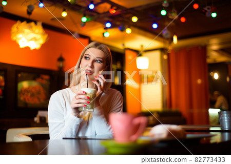 Woman drinking coffee and talks on the phone in a cafe. 82773433