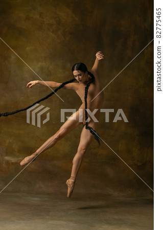 Full-length portrait of beautiful ballerina dancing, flying like a bird isolated over vintage background. Antique style performance 82775465