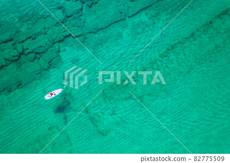 Alone man rowing on SUP board on aquamarine, blue sea water with coral in lagoon. Aerial top view paddleboard. Surfing 82775509