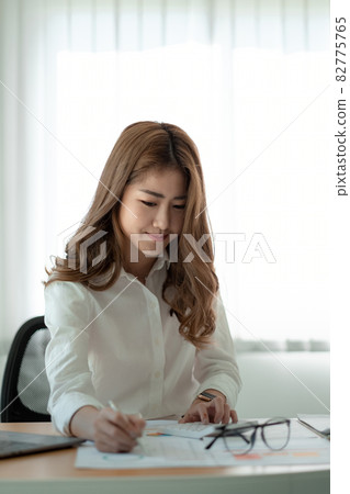 Business asian woman using calculator at working with financial report. she working with laptop computer Business asian woman using calculator at working with financial report. she working with laptop computer 82775765