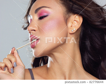 Beautiful close-up portrait of a girl with long curly hair and evening pink makeup. The girl pulls the gum out of her mouth. Extremely long eyelashes and gentle facial skin care Beautiful close-up portrait of a girl with long curly hair and evening pink makeup. The girl pulls the gum out of her mouth. Extremely long eyelashes and gentle facial skin care 82776644
