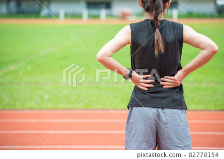 Back view of young runner woman suffering from Backache or Sore waist after running in the running track in stadium. Conceptual of woman suffering painful from sport workout. 82778154