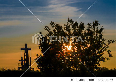 Oil pump and tree at sunset in sun. Gold and blue. 82778276