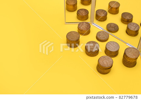 concept of profit growth. a stack of coins near the mirror on a yellow background. copy space. Ukrainian hryvnia 82779678