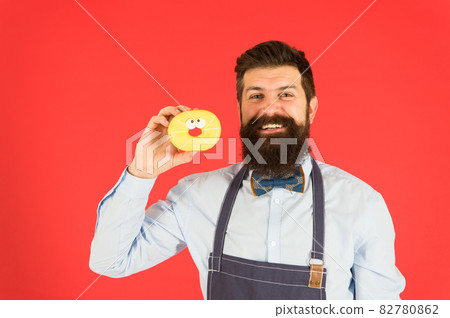 Happy baker. Bearded baker holding doughnut on red background. Happy baker. Bearded baker holding doughnut on red background. 82780862
