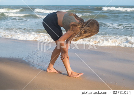 Kneading body muscles after jogging. Blond caucasian Girl massage her leg after jogging outdoors.healthy girl do sport workout by the sea. leg injury Kneading body muscles after jogging. Blond caucasian Girl massage her leg after jogging outdoors.healthy girl do sport workout by the sea. leg injury 82781034