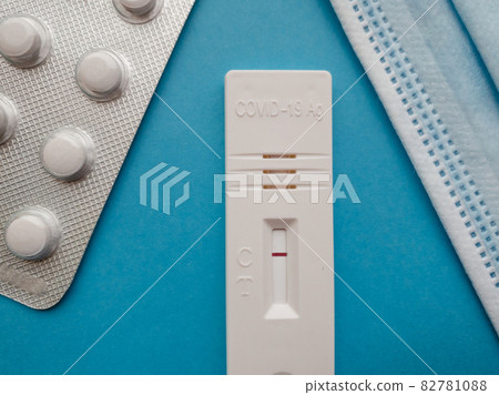 Coronavirus antigen test with a negative result on a blue bright background next to a thermometer, a medical mask, pills and a syringe 82781088